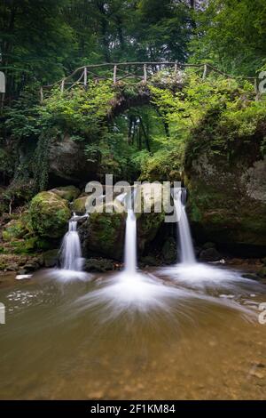 Idyllischer kleiner Wasserfall in üppig grüner Waldlandschaft mit einem Alte Brücke darüber Stockfoto