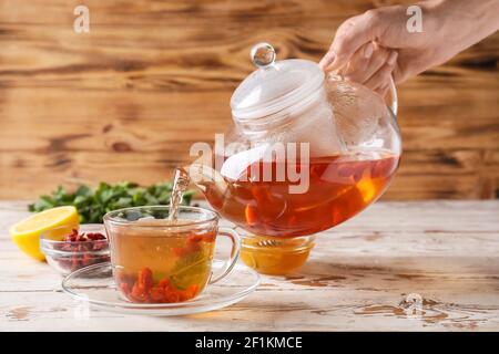 Frau goji Tee aus der Teekanne in die Tasse auf Holz Hintergrund Stockfoto