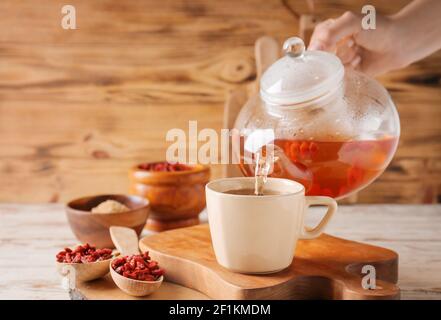 Frau goji Tee aus der Teekanne in die Tasse auf Holz Hintergrund Stockfoto