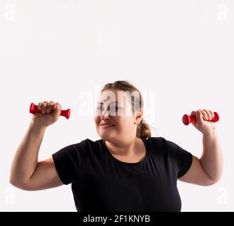 Portrait von kaukasischen Fett, übergewichtig, übergewichtige Frau, Blick auf Kamera mit Lächeln, Übungen mit roten Hanteln für fit gesund, grauen Hintergrund. Stockfoto