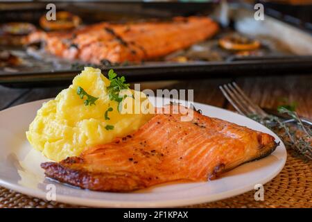 Im Ofen gerasteter Lachs gefüllt mit Kartoffelpüree auf einem Teller mit Backblech im Hintergrund auf dem Küchentisch. Vorderansicht Stockfoto