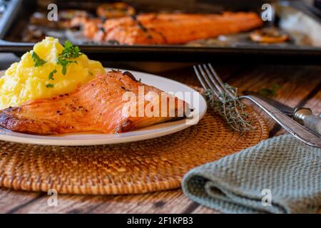 Im Ofen gerasteter Lachs gefüllt mit Kartoffelpüree auf einem Teller mit Backblech im Hintergrund auf dem Küchentisch. Vorderansicht Stockfoto