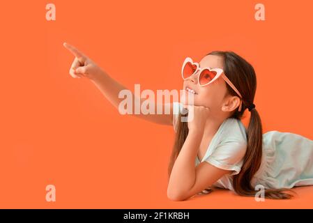 Nettes kleines Mädchen in stilvollen herzförmigen Sonnenbrille auf farbigem Hintergrund Stockfoto