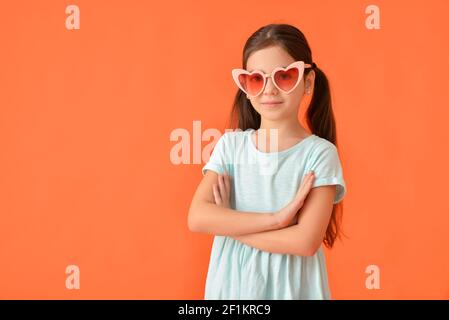 Nettes kleines Mädchen in stilvollen herzförmigen Sonnenbrille auf farbigem Hintergrund Stockfoto