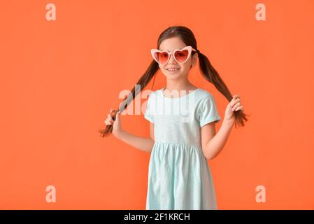 Nettes kleines Mädchen in stilvollen herzförmigen Sonnenbrille auf farbigem Hintergrund Stockfoto