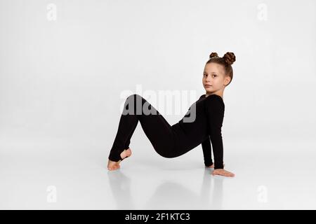 Kleines Kind Mädchen in schwarzer Sportswear tun Stretching auf Studio-Hintergrund. Stockfoto