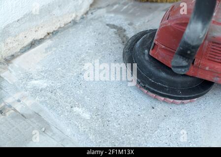 Der Bauarbeiter verwendet einen Betonschleifer zum Entfernen von Fliesenkleber Und Harz bei Renovierungsarbeiten Stockfoto