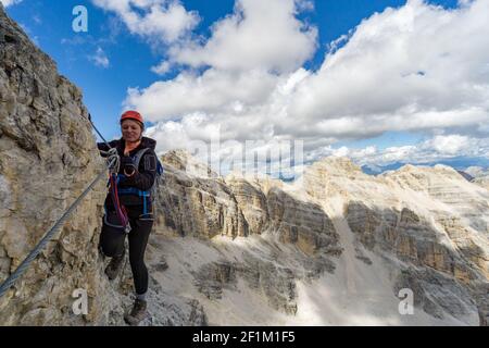 Attraktive blonde Bergsteigerin auf einem steilen Klettersteig In den italienischen Dolomiten Stockfoto