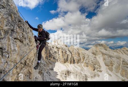 Attraktive blonde Bergsteigerin auf einem steilen Klettersteig In den italienischen Dolomiten Stockfoto