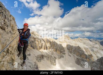 Attraktive blonde Bergsteigerin auf einem steilen Klettersteig In den italienischen Dolomiten Stockfoto