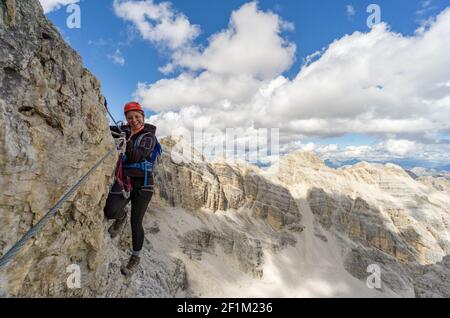 Attraktive blonde Bergsteigerin auf einem steilen Klettersteig In den italienischen Dolomiten Stockfoto