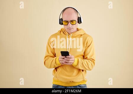 Glatze schöner Mann in gelben Sonnenbrille und Kapuzenpullover hören Musik auf dem Smartphone Stockfoto