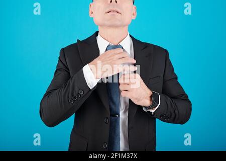 Zugeschnittenes Bild von ernsthaften reifen Unternehmer Anpassung Krawatte, isoliert auf blau Stockfoto