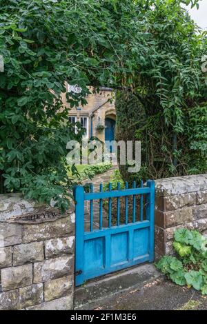 Holztor führt zu einem Vorgarten im Gutsdorf Edensor, Derbyshire, Großbritannien; Tor zeigt die blaue Verkleidung des Chatsworth Estate Stockfoto