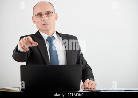 Portrait von seriösen reifen Geschäftsmann in Gläsern sitzen im Büro Tisch und poiting an der Kamera Stockfoto