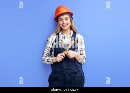 Beschäftigt Ingenieur Konstrukteur Frau Blick auf Kamera Halten in der Hand Einstellbare Werkzeuge, Hammer und ein Schraubendreher Instrumente isoliert über blauem Studio-Bac Stockfoto