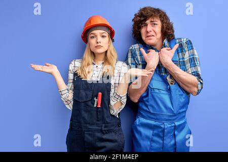 Junge Ingenieure erfüllten den Bauplan nicht richtig, ungelernte Bauarbeiter in Uniform gekleidet isoliert über blauem Studio-Backgroun Stockfoto