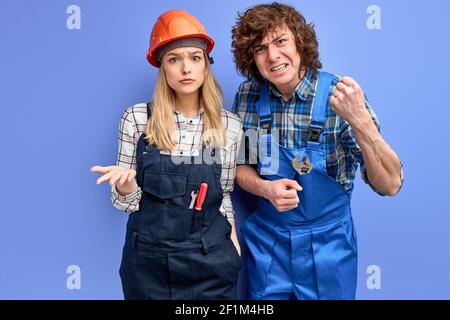 Zwei Vorarbeiter, die mit der Qualität der Reparaturarbeiten des Bauherrn unzufrieden sind, stehen, die Kamera ernsthaft betrachten, wütend unzufriedenen Ausdruck auf Gesicht habend. woma Stockfoto