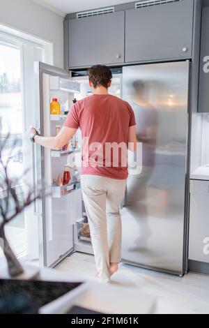 Mann, der vor dem offenen Kühlschrank steht Stockfoto