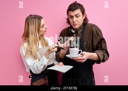 Lead weiblichen Kellner macht Beschwerde gegen einen unerfahrenen männlichen Kellner, haben Gespräch während der Arbeit, erklären, wie man Kundenaufträge nehmen. Isoliert rosa Bac Stockfoto