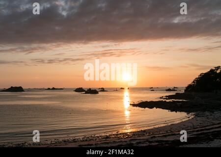 Sonnenuntergang über einer idyllischen Bucht und Strand mit Aussicht Des Ozeans und felsigen Riffen unter einem bunten Himmel Stockfoto