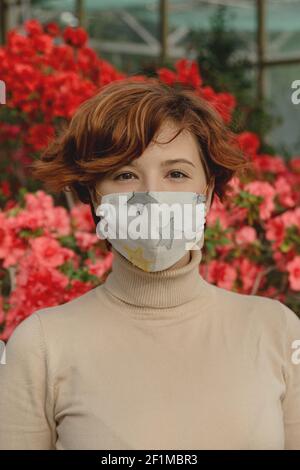 Eine schöne Frau, die eine schützende Gesichtsmaske zwischen Frühlingsblumen trägt. Stockfoto