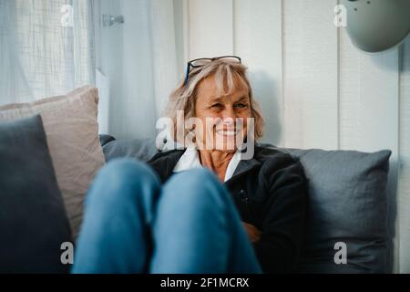 Lächelnde ältere Frau sitzt auf dem Sofa Stockfoto