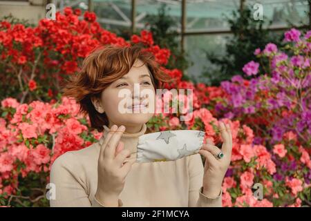 Eine schöne Frau entfernt schützende Gesichtsmaske und inhaliert unter Frühlingsblumen Stockfoto