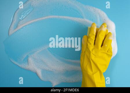 Weibliche Hand in schützenden gelben Handschuh, Schwamm und Schaum auf blauem Hintergrund. Hausreinigungskonzept. Draufsicht. Speicherplatz kopieren Stockfoto