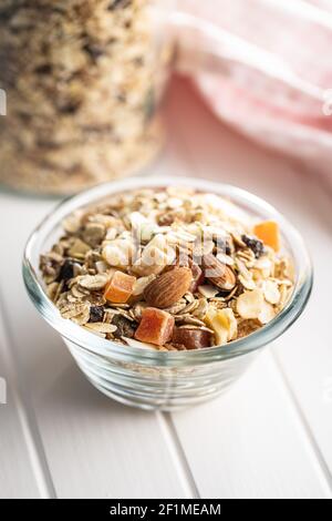 Frühstücksflocken in einer Schüssel. Gesundes Müsli mit Haferflocken, Nüssen und Rosinen auf weißem Tisch. Stockfoto