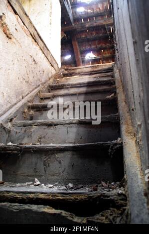 Alte Dachtreppe in einem ruinierten Gebäude. Eine dunkle und geheimnisvolle Ecke eines schmutzigen Hauses. Stockfoto