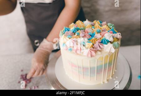 Ein Konditor macht mit eigenen Händen einen Hochzeitstorte und setzt bunte Dekorationen mit Sahne auf die Kuchen. Vorbereitung auf die Feier Stockfoto