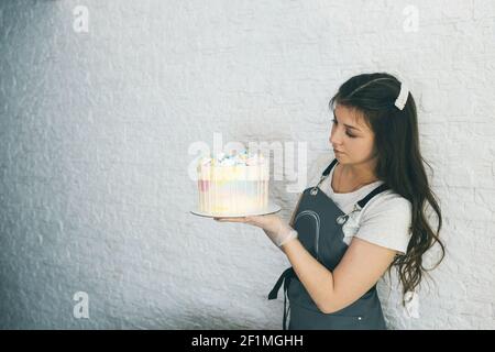 Ein Konditormädchen hält einen vorbereiteten Kuchen in ihren Händen. Stockfoto