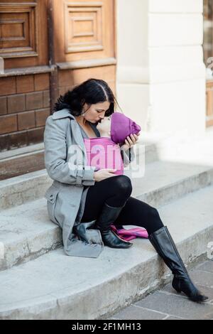 Portrait der liebevollen Babytragemutter trägt ihr Kind in der Stadt Stockfoto