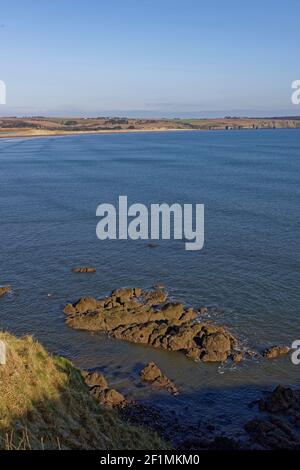 Einige der roten Sandsteinfelsen, die von der Ebbe an der Lunan Bay freigelegt wurden, mit den Wellen der zurücktretenden Flut, die sanft gegen sie schlagen, Stockfoto