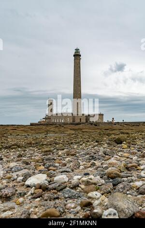Hoher Leuchtturm aus Stein mit felsiger Küste bei Ebbe unter Ein stürmischer Himmel Stockfoto