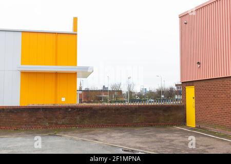 Leuchtend gelbe, rosa gewellte Lagereinheiten, Ziegelwand. Auf dem alten Viehmarkt (Freimens Gemeinsamer Industriepark) zeigt die Zählerhausuhr. Stockfoto