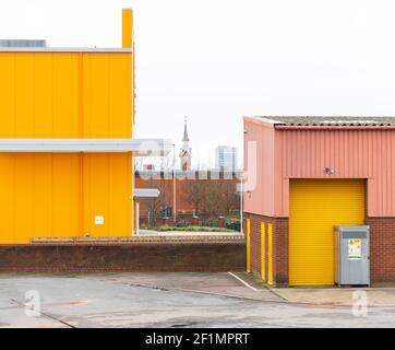 Leuchtend gelbe, rosa gewellte Lagereinheiten, Ziegelwand. Auf dem alten Viehmarkt (Freimens Gemeinsamer Industriepark) zeigt die Zählerhausuhr. Stockfoto