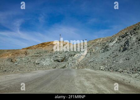 Kupfererz im Tagebau. Panorama des Steinbruchs. Grüner Boden, Schotterstraße auf blauem Himmel Hintergrund. Kommunikationsturm und Beleuchtungsmast. Stockfoto