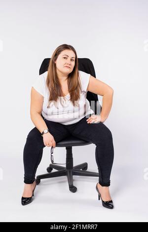 Frau im Büro. Kaukasische plump Frau sitzt in Ledersessel posiert auf weißem Hintergrund Blick auf die Kamera. Stockfoto
