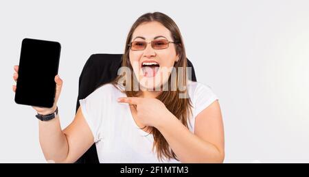 Glücklich plus Größe Frau blogger. Zeigt es der Kamera an und zeigt mit dem Zeigefinger auf den schwarzen Bildschirm. Weißer Studiohintergrund und Seitenraum. Stockfoto