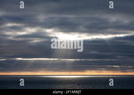 Die Sonne bricht durch stürmische Wolken über dem Meer vor Cornwall, Großbritannien Stockfoto