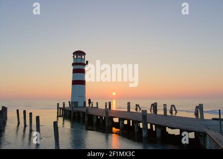 Die Sonne geht hinter dem Leuchtturm von Podersdorf unter und spiegelt sich am zufroren Neusiedlersee in Österreich. Stockfoto