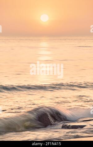 Friedlicher Sonnenaufgang am Strand, selektiver Fokus auf Felsen, Langzeitbelichtung. Stockfoto