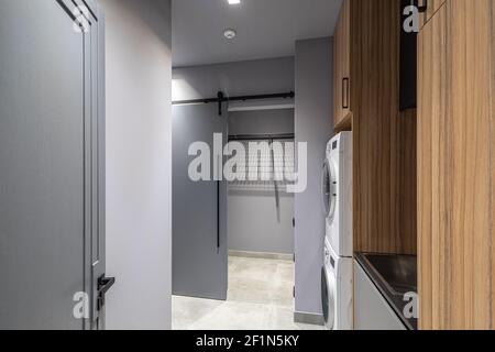 Modernes Interieur der leeren Waschküche in Luxus-Privathaus. Grautöne. Holzschränke. Waschmaschine. Stockfoto