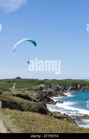 Gleitschirm fliegen über einem malerischen Sandstrand auf te felsigen Küste der Bretagne Stockfoto