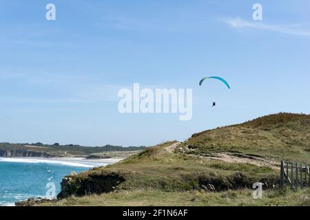 Gleitschirm fliegen über einem malerischen Sandstrand auf te felsigen Küste der Bretagne Stockfoto