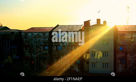 Good Morning Yangon: Sonnenstrahl auf dem Dach von Flachbauten mit einer Silhouette eines einzigen fliegenden Vogels, während die Sonne in der Hauptstadt der Stadt Myanmar aufgeht Stockfoto