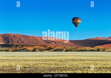 Heißluftballon mit Reisenden, die über rote Sanddünen fliegen. Der Ballon ist am blauen Himmel. Sossusvlei, Namib Naukluft Nationalpark, Namibia, Afrika Stockfoto