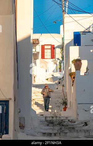 Ein Mann geht die Stufen hinunter bei gewaschenem Weiß Enge Gassen mit Fenstern und Türen an einem sonnigen Tag Mit blauem Himmel auf einer griechischen Insel Stockfoto